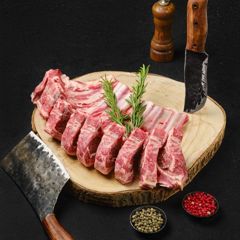 Raw lamb rib roast on wooden slab and butcher cleaver